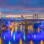 Minneapolis skyline and I-35W bridge lit up at night, reflecting over the Mississippi River.