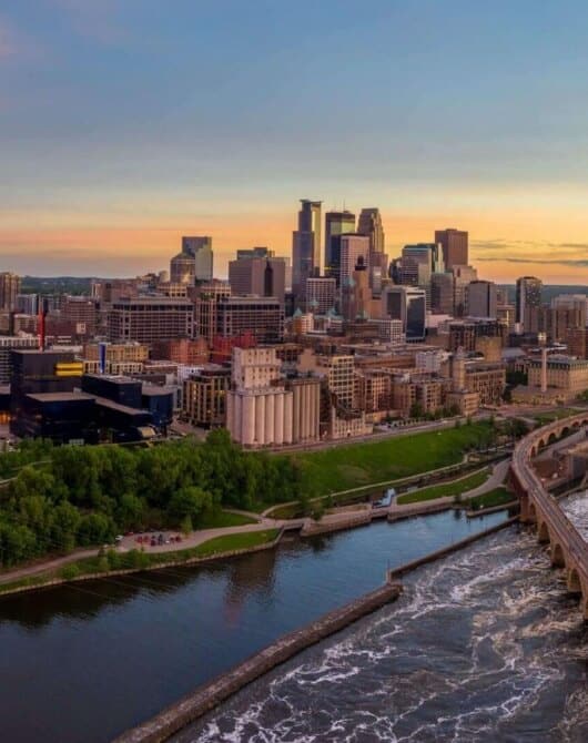 Aerial view of downtown Minneapolis, Minnesota skyline during sunset with the Mississippi River in the foreground.