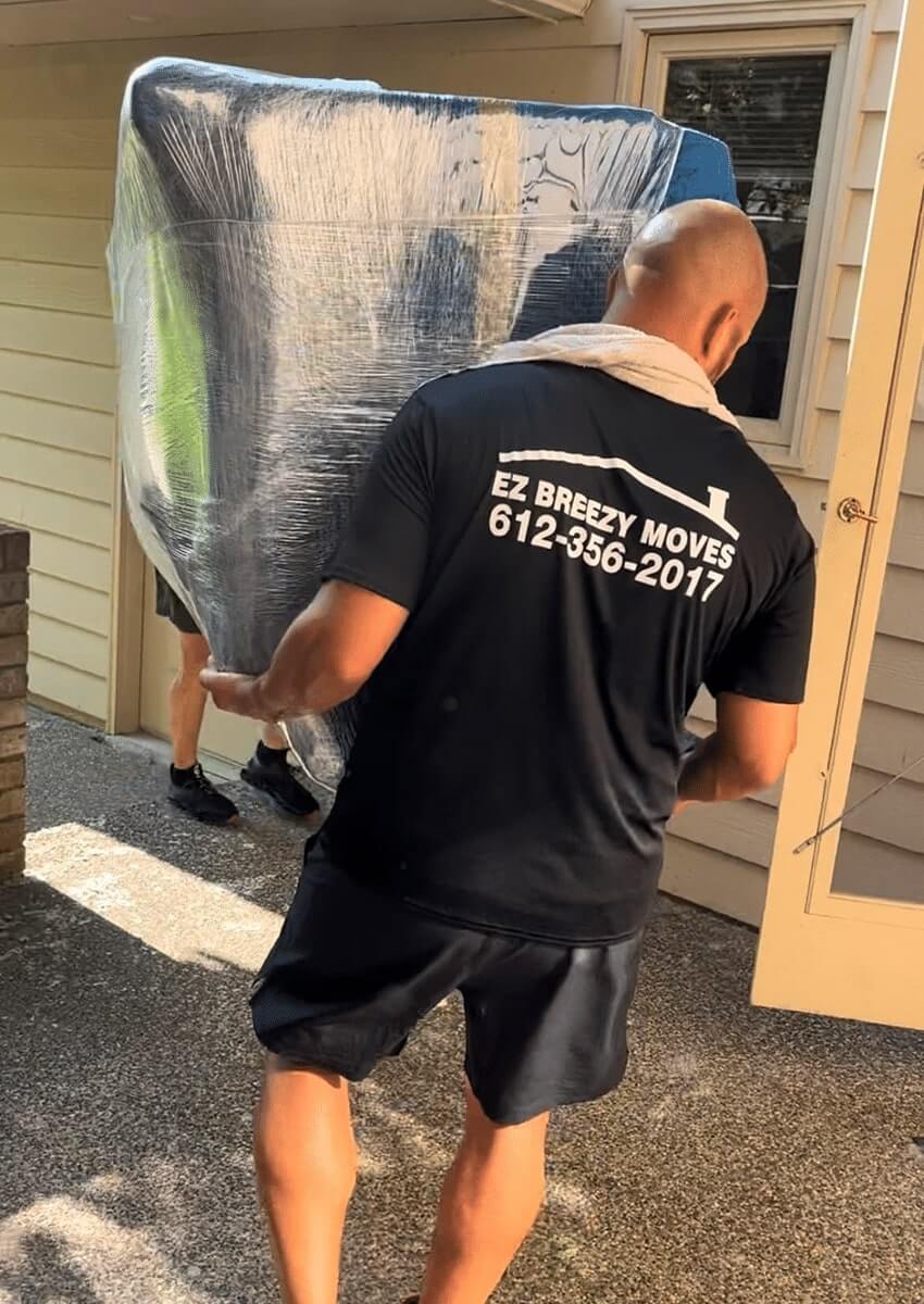 EZ Breezy Moves crew member delivering professional Minneapolis moving services while carrying a wrapped couch in North Loop, MN.