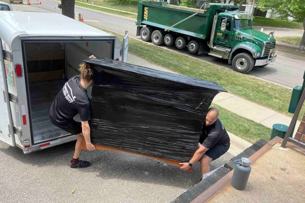 Two EZ Breezy movers carefully loading shrink-wrapped furniture into a moving truck in Edina, MN.