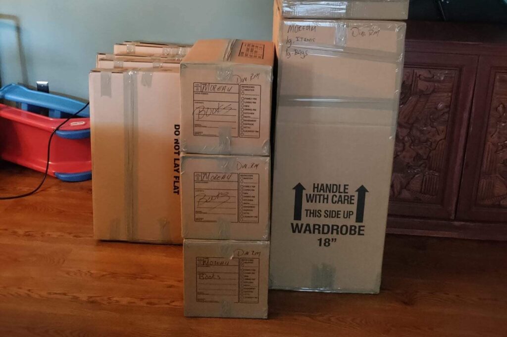 A close-up view of a wardrobe box and other labeled moving boxes for books, highlighting the organized process that our Labor Only Movers Twin Cities team complements with professional moving labor.