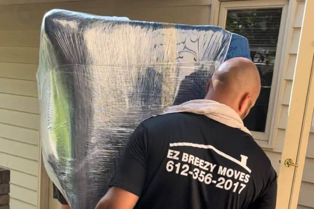 EZ Breezy Movers professional carefully moving shrink-wrapped furniture in St. Paul.
